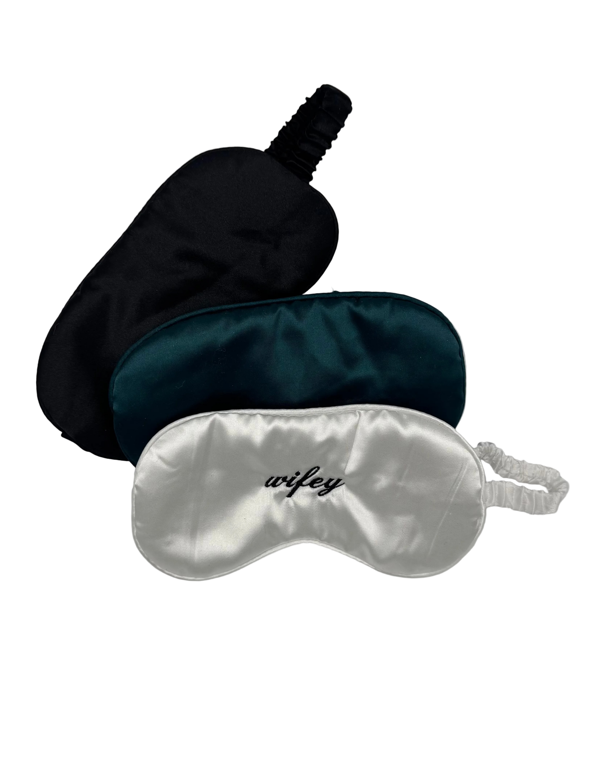 Three satin sleep masks in black, green, and silver on a light gray background.