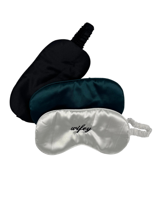 Three satin sleep masks in black, green, and silver on a light gray background.